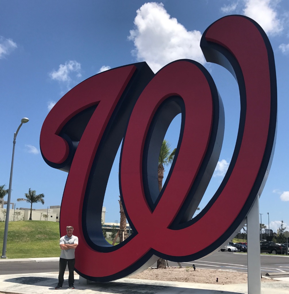 Benny Gallo standing full-body in front of the Washington Nationals emblem at Nationals Headquarters